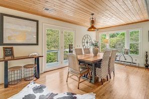 Enjoy meals in this inviting dining area with a wooden table and wicker chairs, surrounded by lush greenery views.