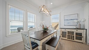 A dining room with a wooden table, white chairs, a bench, a chandelier, a cabinet with glass doors, and a painting on the wall. - Spectacular Ocean Front home (Flagler Beach)