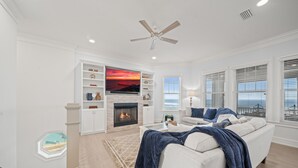 A modern living room with a fireplace, white sofas, a coffee table, and a large TV. - Spectacular Ocean Front home (Flagler Beach)