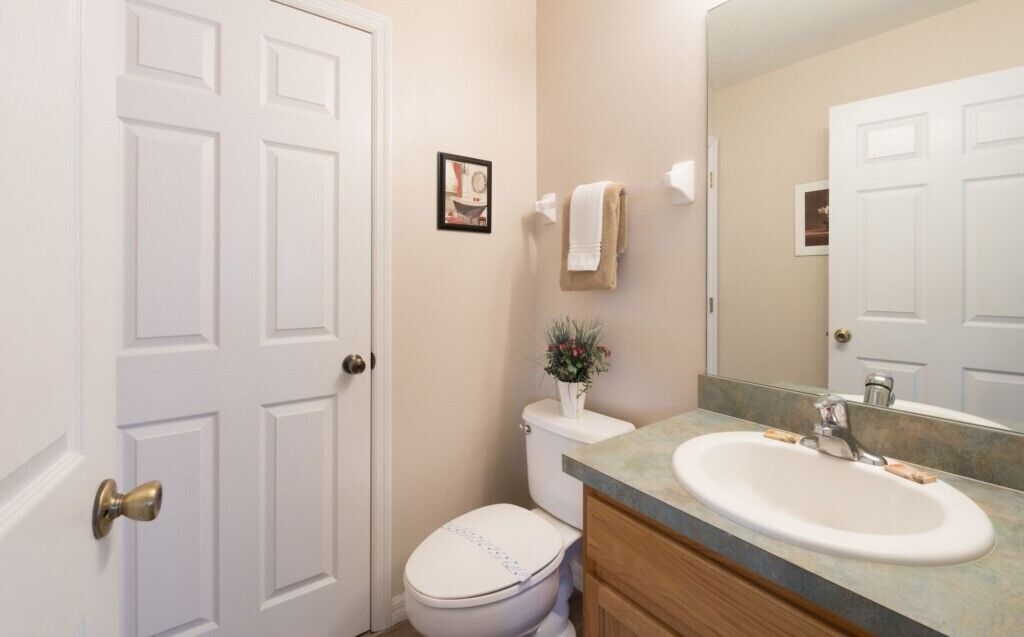 A bathroom with a white toilet, a sink with a mirror, and a door with a brass handle.