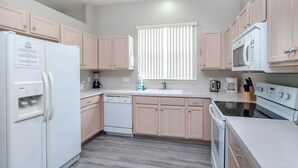 A modern kitchen with light wood cabinets, a white refrigerator, a dishwasher, a microwave, and an oven. - Elegant 4BR Villa w/ Private Pool & Spa near Disney - Backs Onto Conservation! (Davenport)