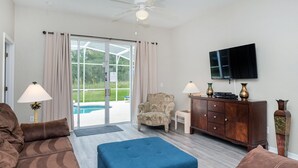 A living room with a sofa, ottoman, armchair, TV, and a cabinet. - Elegant 4BR Villa w/ Private Pool & Spa near Disney - Backs Onto Conservation! (Davenport)