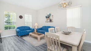 A living room with two blue sofas, a wooden coffee table, a dining table with chairs, and a chandelier. - Elegant 4BR Villa w/ Private Pool & Spa near Disney - Backs Onto Conservation! (Davenport)