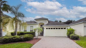 A residential house with a driveway, garage, and well-maintained landscaping including bushes and a palm tree. - Elegant 4BR Villa w/ Private Pool & Spa near Disney - Backs Onto Conservation! (Davenport)