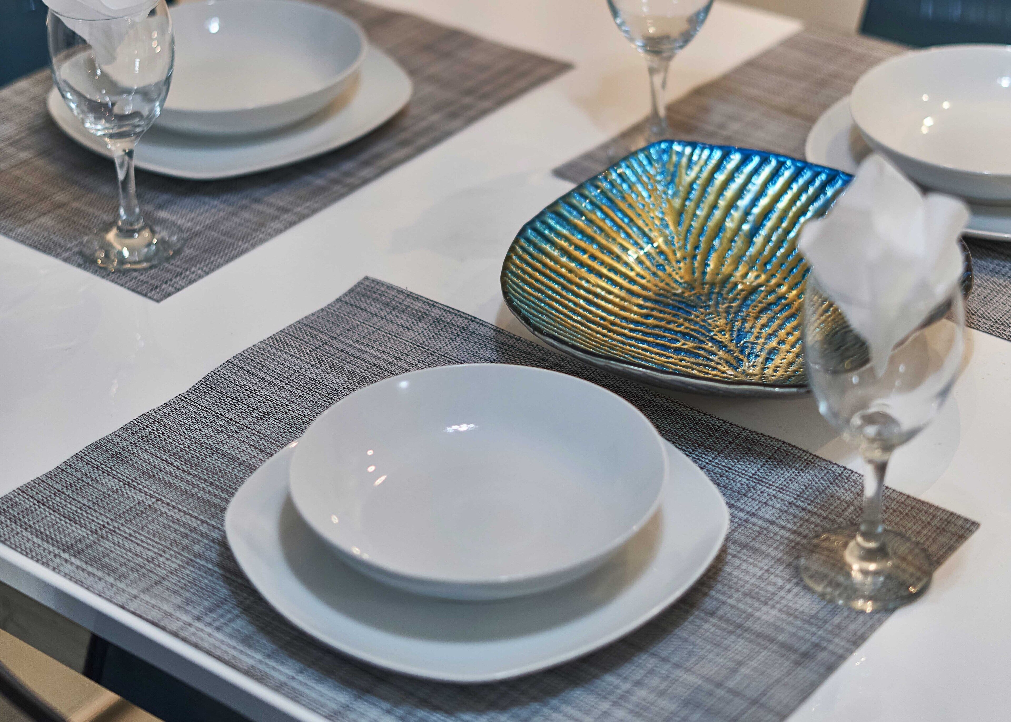 A table set with white plates, a decorative blue and gold bowl, and clear glasses.