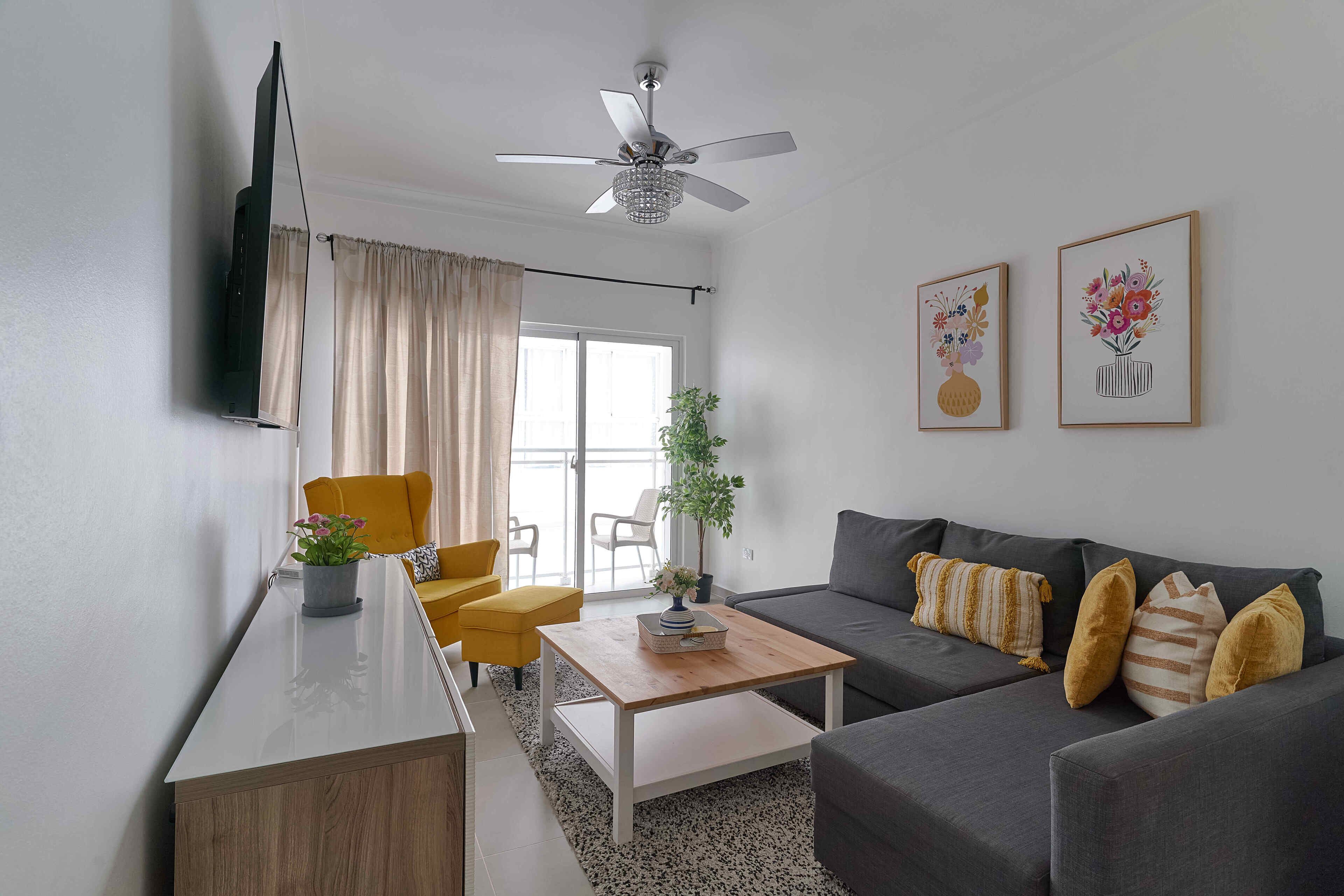 A modern living room with a sofa, a coffee table, a TV mounted on the wall, and a ceiling fan.