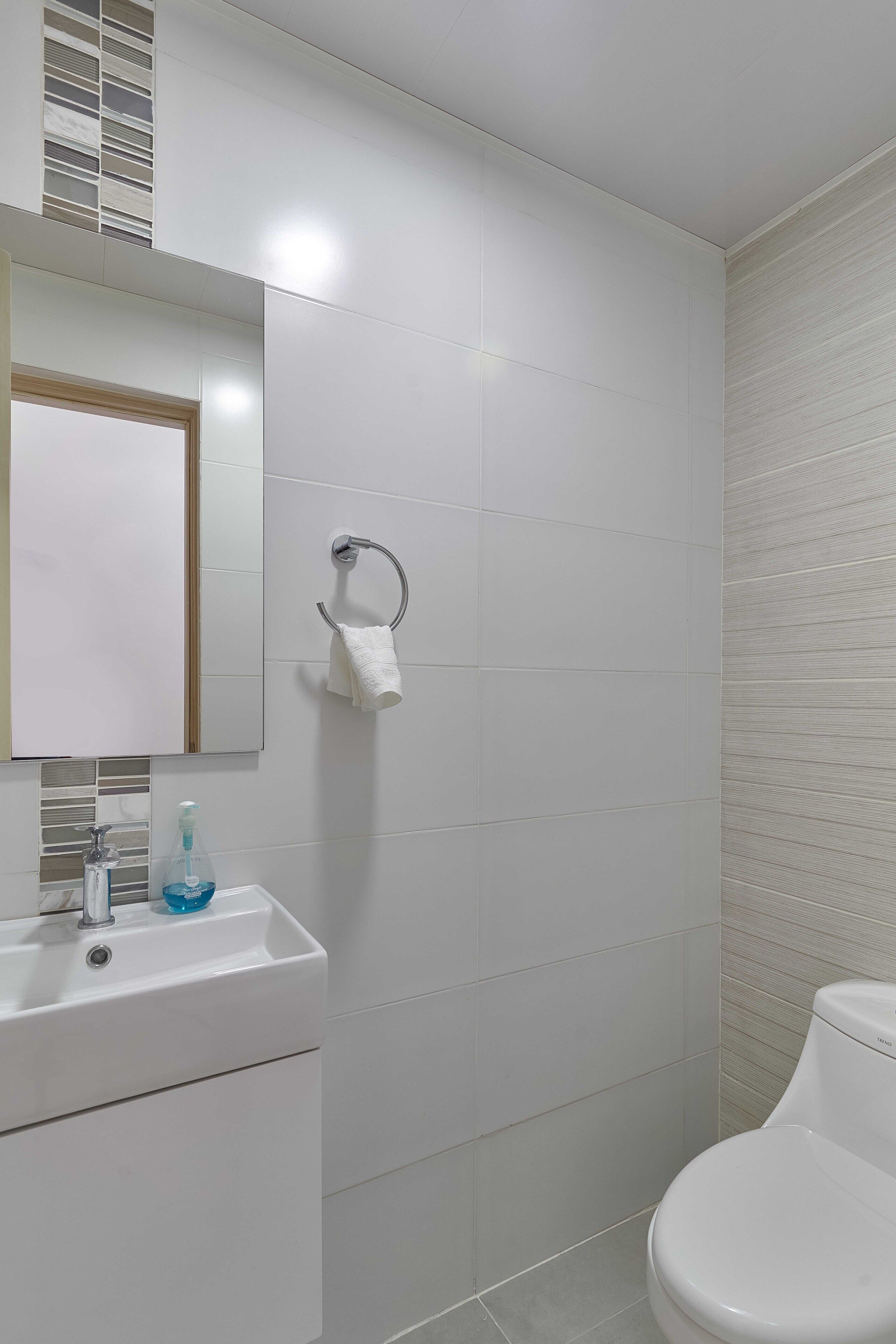A bathroom with white tiles, a sink with a mirror, a towel rack, and a toilet.