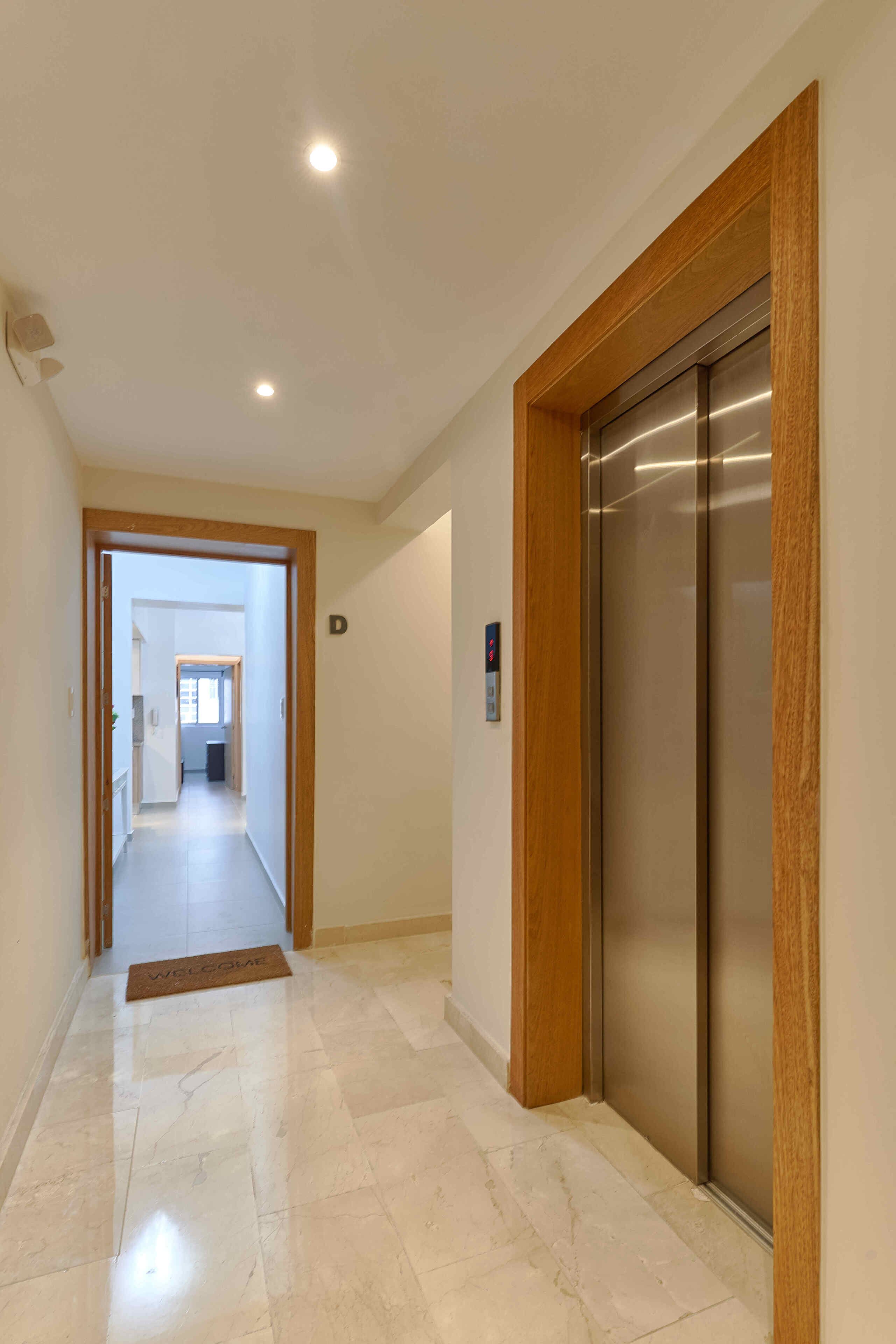 A hallway with a polished marble floor, a welcome mat, and a modern elevator.