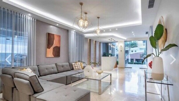 Un salon moderne avec un canapé d’angle, une table basse en verre et des luminaires suspendus.