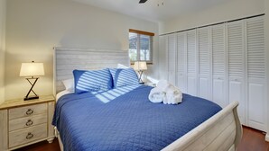 Ein ordentlich bezogenes Bett mit einer blauen Steudecke, einem weißen Kopfteil und einem Deckenventilator.