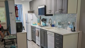 Cozinha moderna com armários cinza, micro-ondas e lava-louças. Um tapete azul no chão e uma cesta com toalhas.