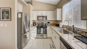 A modern kitchen with stainless steel appliances, white cabinetry, a granite countertop, and a window with blinds. - Clean, Convenient & Comfortable Vegas House (Las Vegas)