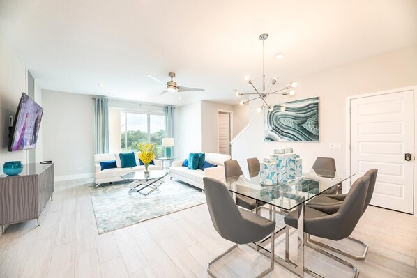 A modern living room with a glass dining table, white sofas, and a ceiling fan.