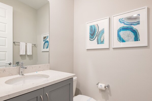Une salle de bain avec un lavabo blanc, un miroir et deux tableaux abstraits encadrés accrochés au mur.