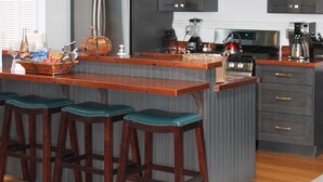 A modern kitchen with dark cabinetry, a central island with bar stools, hanging pendant lights, and a microwave above the island. - Treat yourself to Luxury (Delta)