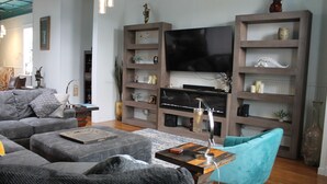 A modern living room with a large flat-screen TV, grey sofas, a teal armchair, and wooden shelves with decorative items. - Treat yourself to Luxury (Delta)