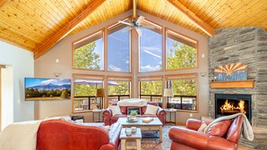 A spacious living room with leather sofas, a fireplace, large windows, and a stone wall.