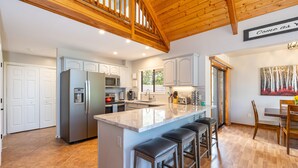 A spacious kitchen with a large island, stainless steel appliances, and a wooden ceiling.