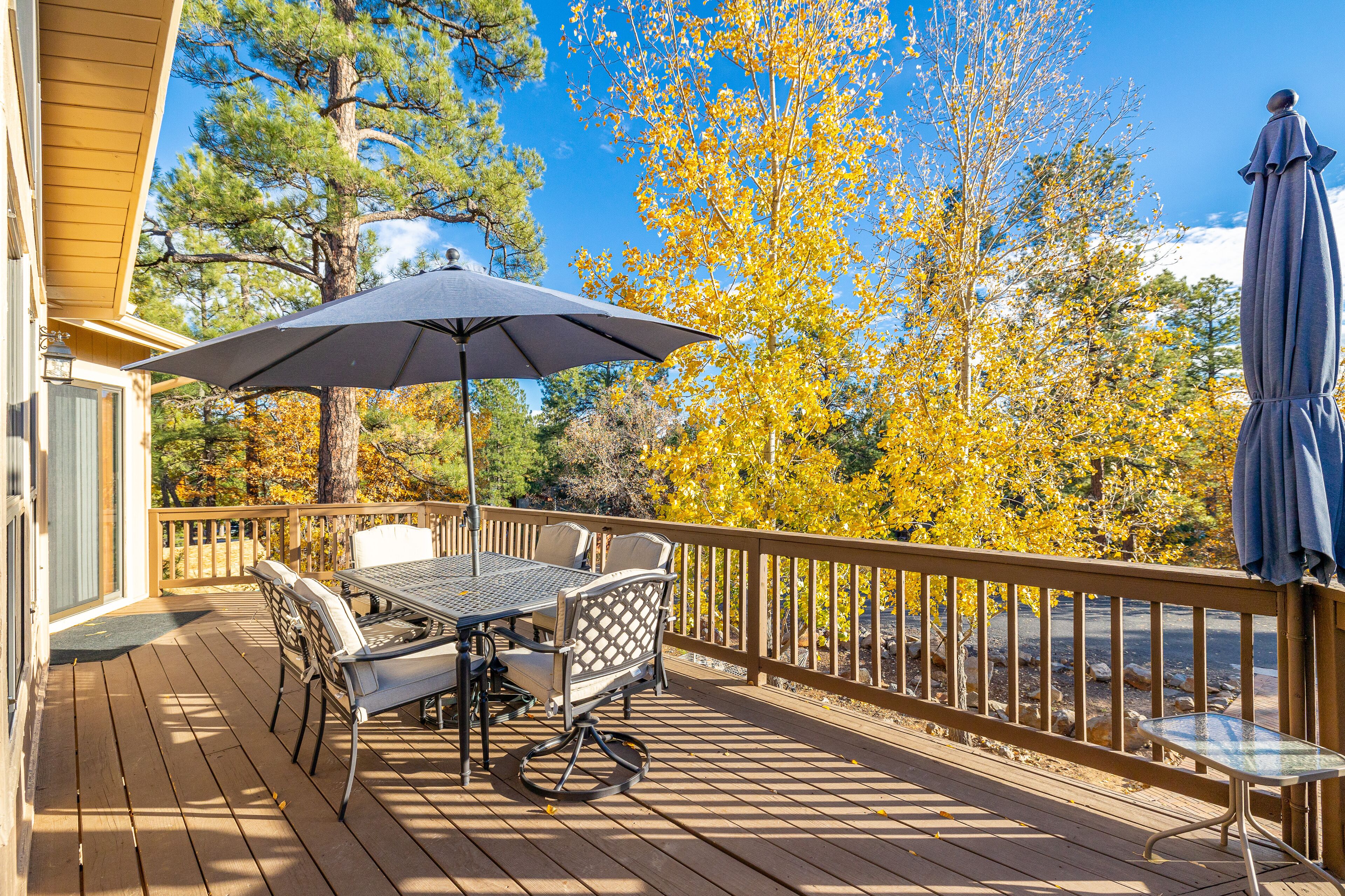 A wooden deck with a table and chairs, a table umbrella, and a view of autumn trees.