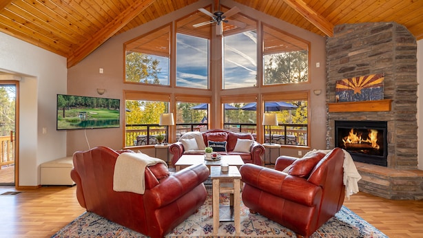 A spacious living room with a stone fireplace, leather sofas, a large TV, and a view of the outdoors.