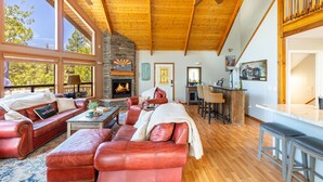 A spacious living room with leather sofas, a fireplace, wooden ceiling, and large windows.