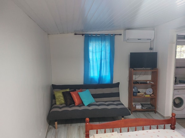 A small, compact room with a single bed, a wooden nightstand, a television, and a washing machine.