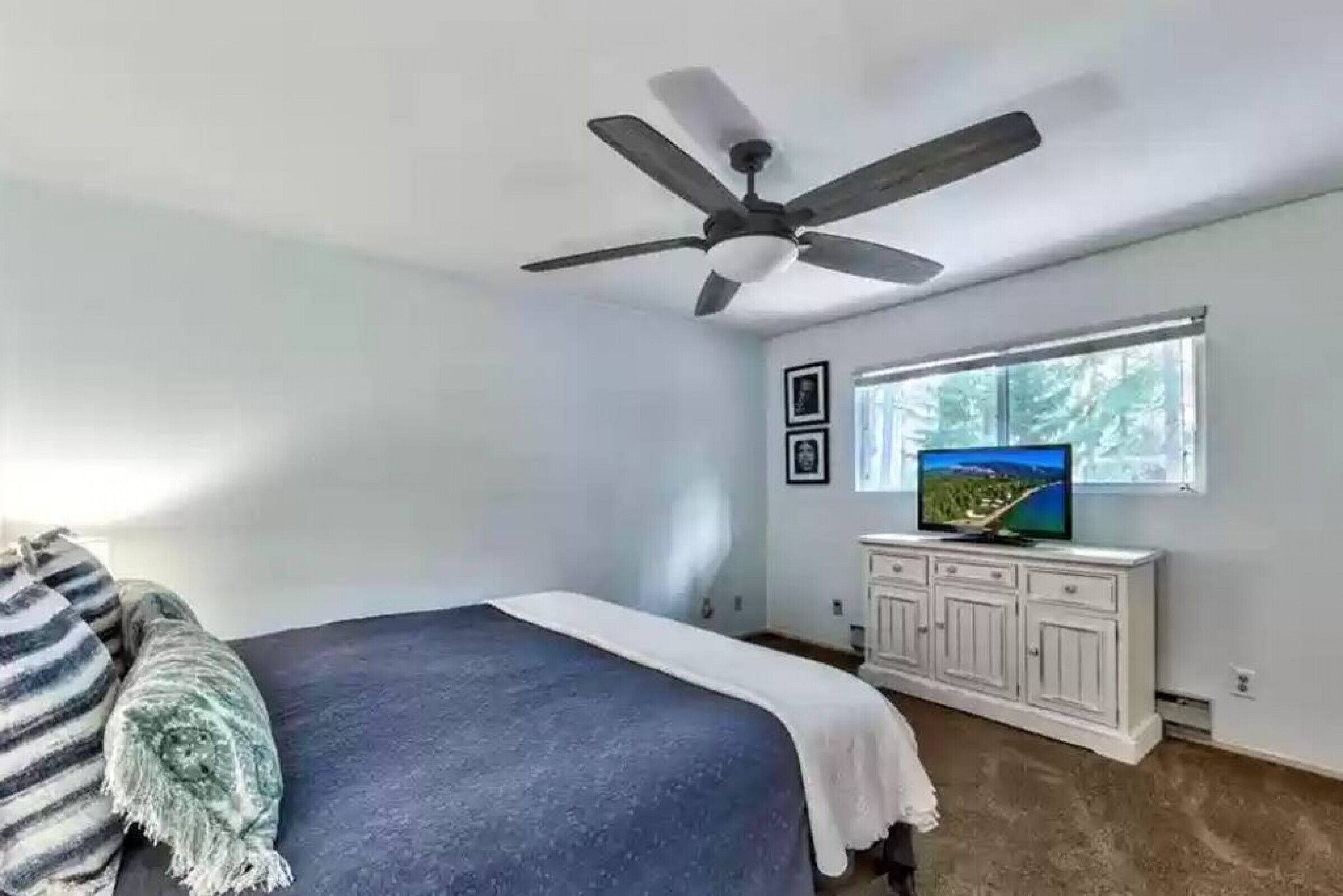 Una camera da letto con un letto, una ventola a soffitto, una televisione su un mobile e una finestra con vista.