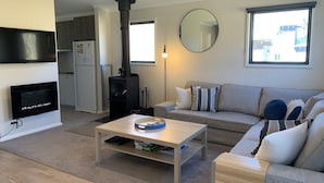 Moderni olohuone, jossa on takka, sohva, sohvapöytä ja suuri ikkuna.