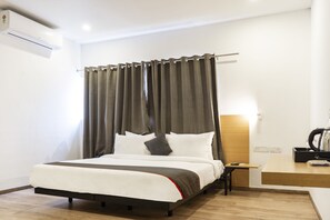 Una habitación de hotel moderna con cama, cortinas, mesita de noche, escritorio y aire acondicionado.