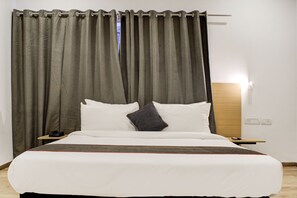 Una habitación de hotel con cama, cortinas, una mesita de noche y un buró.