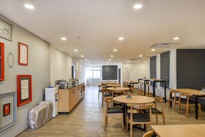 Un comedor amplio con varias mesas y sillas, una encimera de cocina con electrodomésticos y cuadros en las paredes.