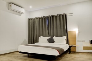 Una habitación de hotel con cama, mesita de noche, escritorio, aire acondicionado y cortina.