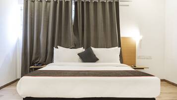 A neatly made bed with a white and brown bedspread, a wooden nightstand with a lamp, and a window with curtains.