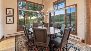 A dining area with a round table and chairs, large windows with a view, and framed pictures on the wall.