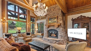 A cozy living room with a stone fireplace, large windows, and a chandelier.