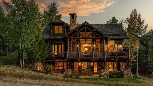 A large, multi-story log cabin with a prominent balcony and stone chimney.
