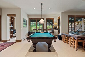 Una mesa de billar en una habitación con ventanas amplias, un banco de madera y una lámpara.