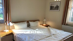 Ein Doppelbett mit weißer Bettwäsche, zwei Nachttische mit Lampen, eine Heizung und ein gerahmtes Bild an der Wand.