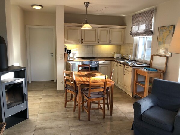 A compact kitchen with wooden cabinets, a dining table with chairs, a stove, and a sofa.