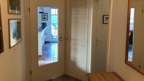 A hallway with a door leading to a kitchen area, a wooden bench, and a mirror on the wall. - Stromstrasse 2 Whg. 26 "Boddenblick" - maisonette apartment in Mediterranean style (Zingst)