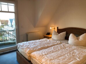 A bedroom with two beds, a nightstand, a lamp, and a view of the outside.