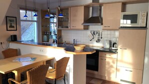 A kitchen with a dining area, featuring a built-in microwave, a coffee maker, and a window with a view. - Stromstrasse 2 Whg. 26 "Boddenblick" - maisonette apartment in Mediterranean style (Zingst)