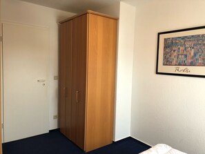 A room with a wooden wardrobe, a bed, and a framed artwork on the wall.