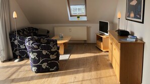 A cozy living room with a sofa, a small table, a TV, and a desk with a lamp. - Hafenstrasse 22 Whg. 7 - Comfortable apartment (Zingst)