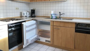 A compact kitchen with wooden cabinets, a built-in oven, a dishwasher, and a coffee maker. - Hafenstrasse 22 Whg. 7 - Comfortable apartment (Zingst)