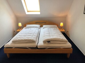 A double bed with a wooden headboard, two bedside tables with lamps, and a skylight above.