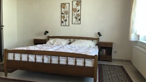 A bedroom with a wooden bed, two nightstands, a bedside table, a patterned rug, and two wall-mounted flower art pieces.