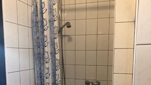 A shower with a curtain, tiled walls, and a handheld showerhead.