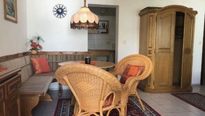A dining area with a round table, two wicker chairs, a bench, and a wooden cabinet.