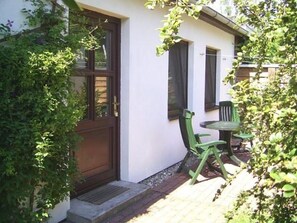 A white building with a wooden door and windows, a small outdoor seating area with a table and chairs, and a brick pathway leading to the entrance. - Klosterstrasse 20 ground floor zfw/011 - small, simple vacation accommodation (Zingst)